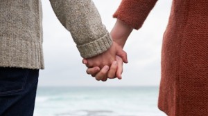 Close up of couple holding hands on coastline.